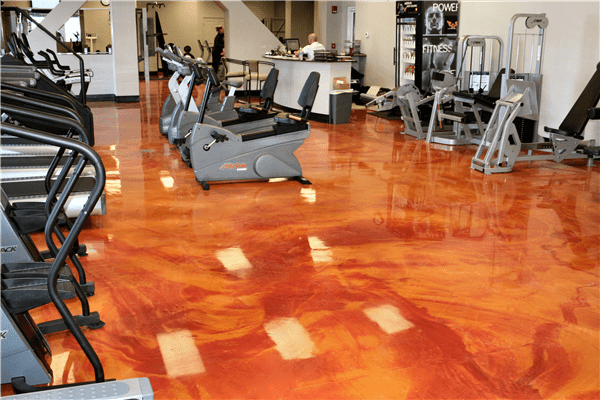 A gym with several machines and a floor that has orange color.